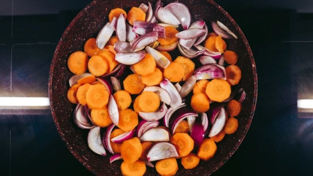 Koekenpan met wortels en uien op kookplaat