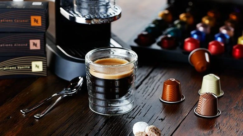 Nespresso-apparaat met glas koffie en cups

