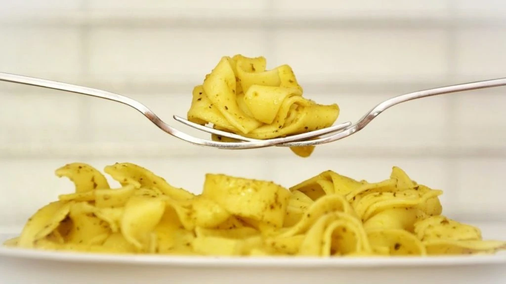 Pasta op twee vorken boven een bord met meer pasta