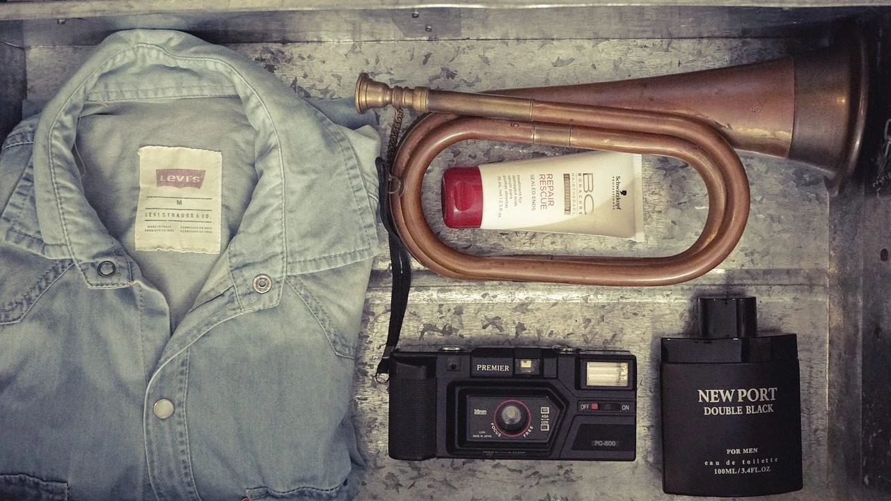 Blouse, muziekinstrument, tube, fototoestel en parfum in kist, bovenaanzicht