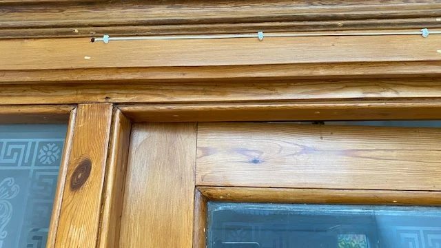 Deurbeldraad met kabelclips op houten deurframe, vooraanzicht.