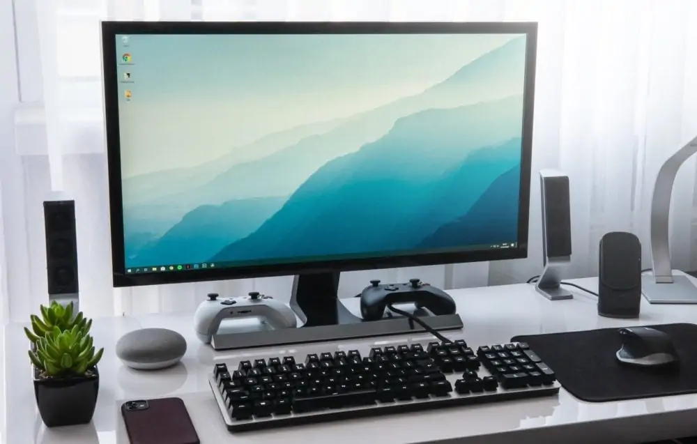 Desktop computer met speakers, toetsenbord, muis en muismat, plantje. Vooraanzicht