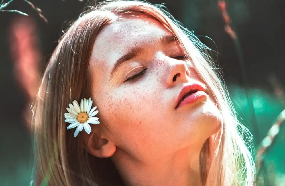 Vrouw met bloem in haar, in de zon. Vooraanzicht, close-up