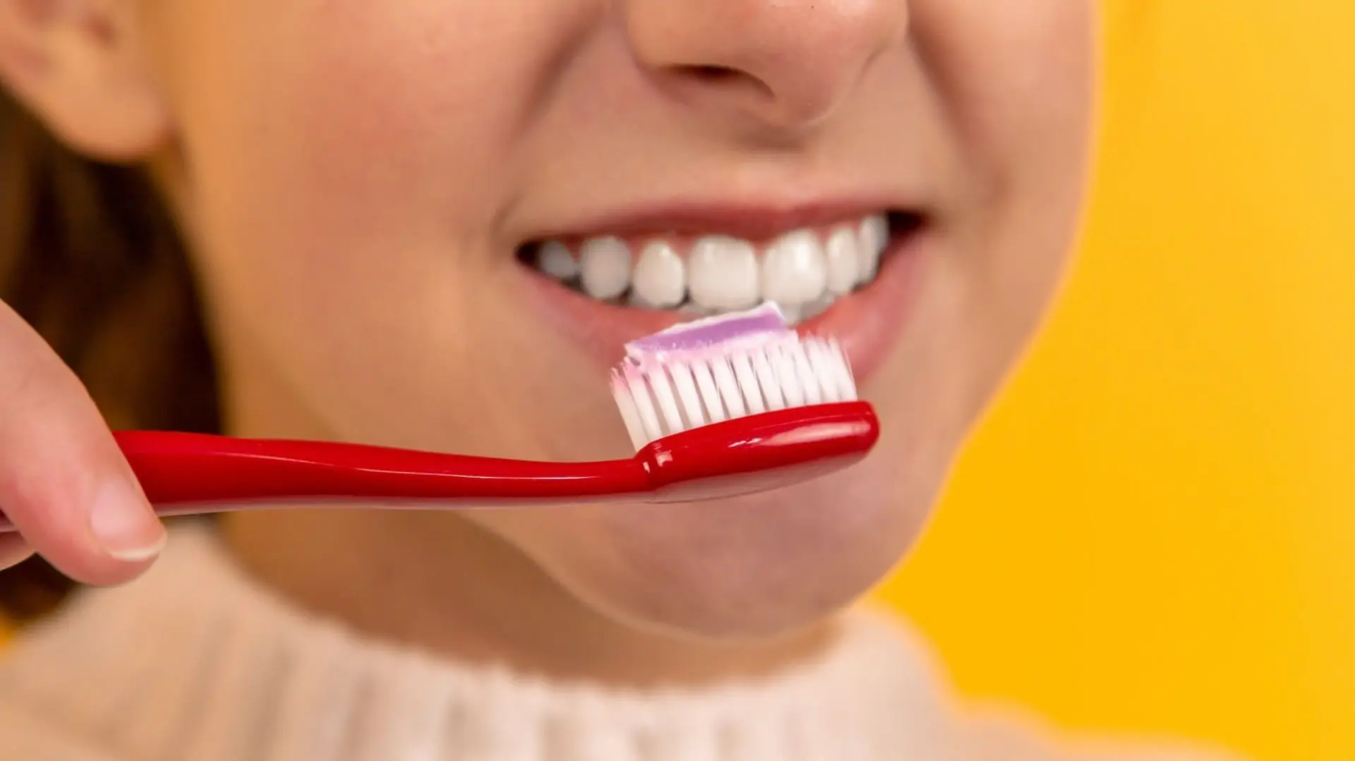 Persoon met brede lach en tandenborstel met tandenpasta op gele achtergrond. Vooraanzicht.
