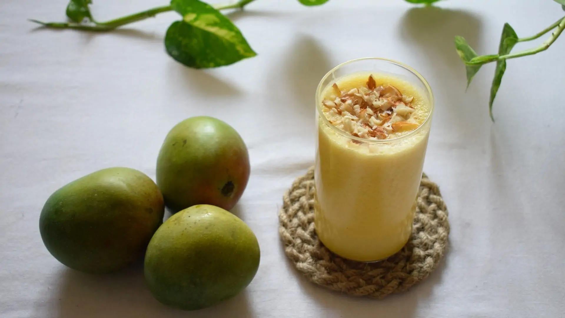 Fruitshake in glas met drie mango's ernaast.