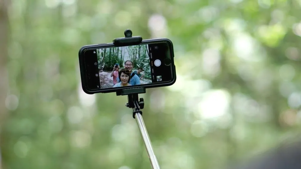 iemand neemt foto van telefoon in selfie stick waarop familie van 3 te zien is