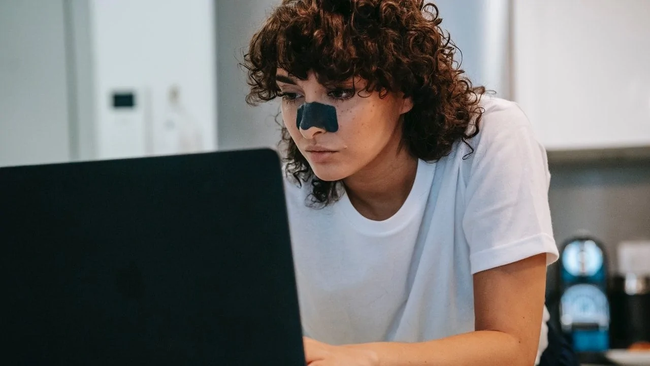 Vrouw met een neusstrip op haar neus voor een laptop.