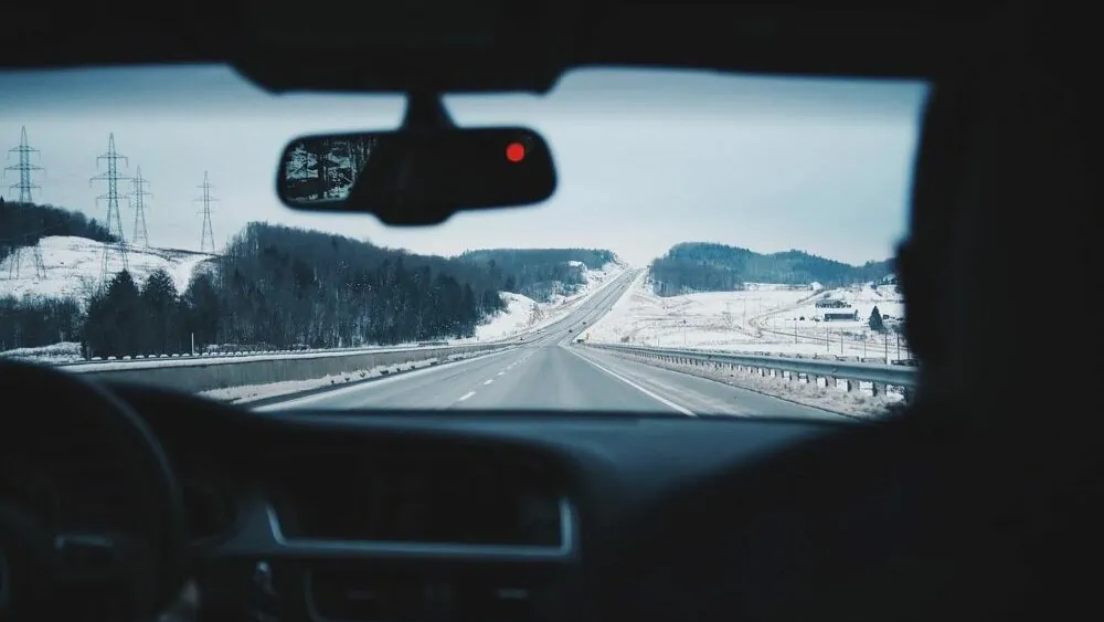 Uitzicht in de auto met achteruitkijkspiegel voor de autoruit, sneeuw. Vooraanzicht