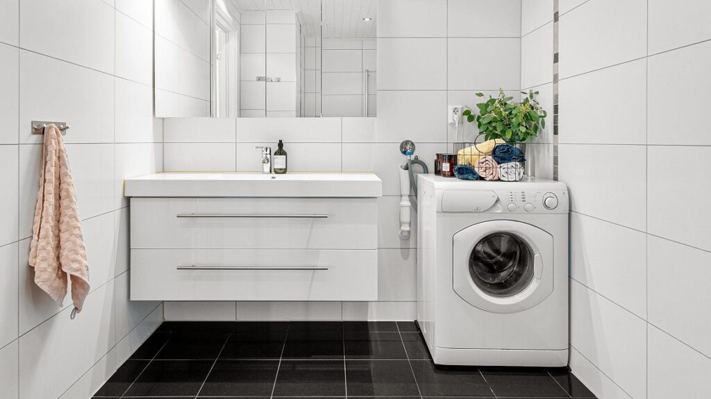 Witte front load wasmachine in wit/zwarte badkamer naast wasbak