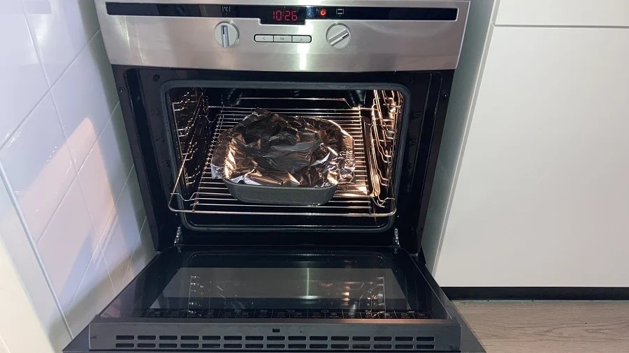 Ovenschaal afgedekt met aluminiumfolie in een openstaande oven. 